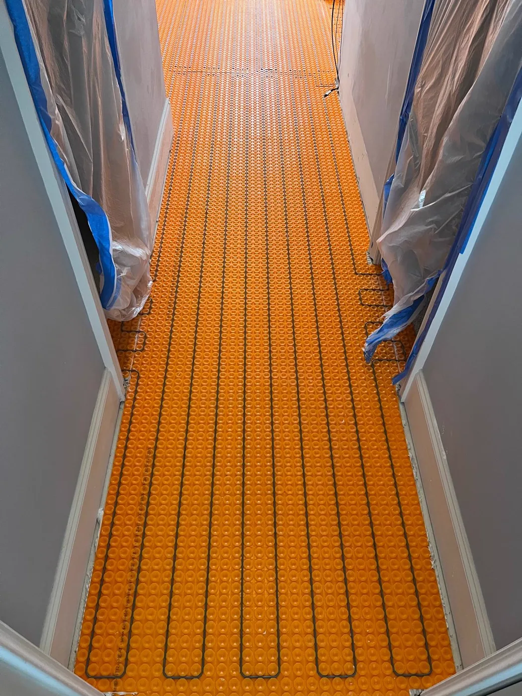 Heated floor system installed before tile, orange heating membrane and cables laid across the subfloor, master bathroom remodel, Metro Atlanta