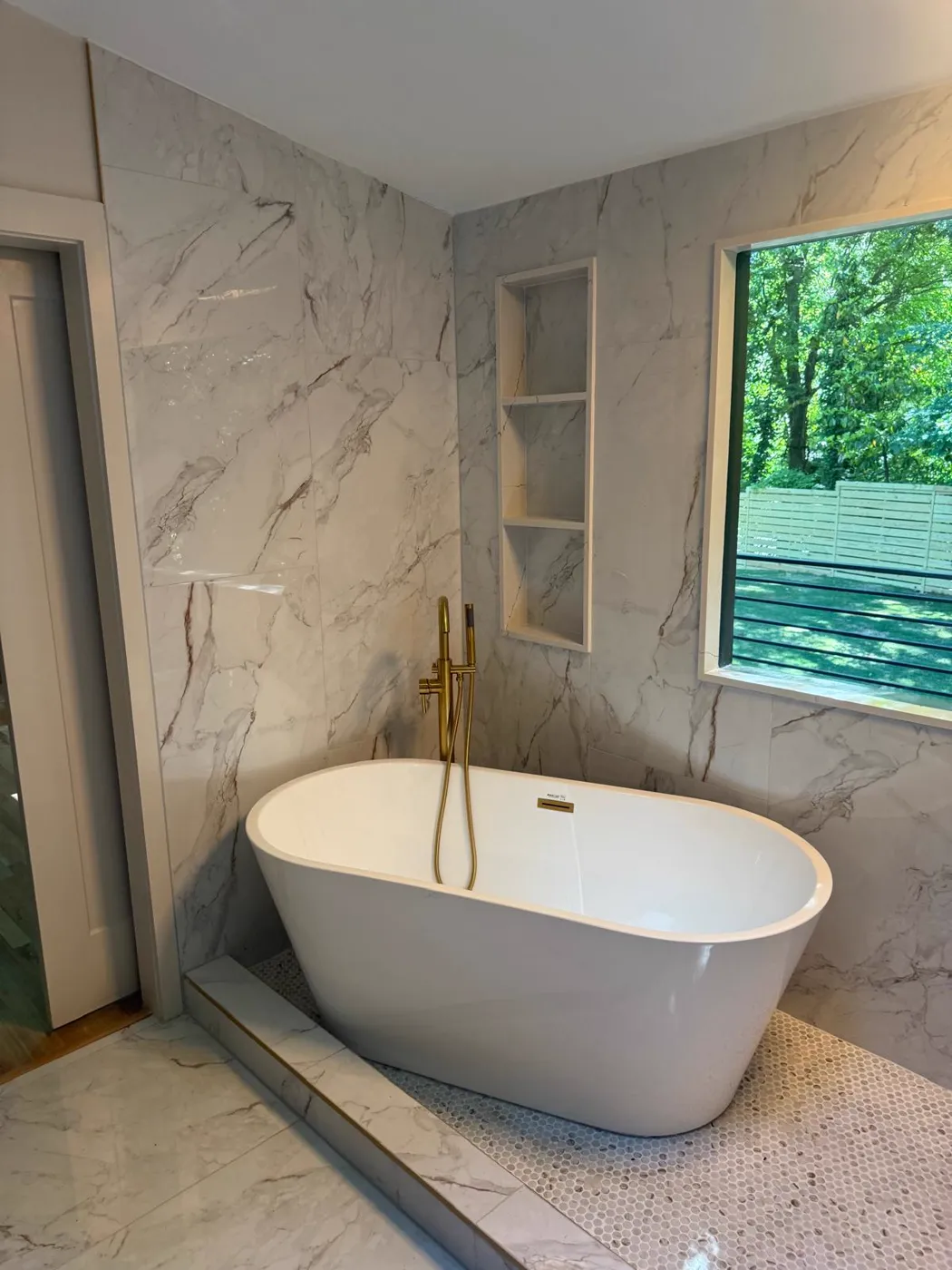 Freestanding soaking tub with a gold floor-mounted filler, marble-look walls and a built-in niche, Metro Atlanta