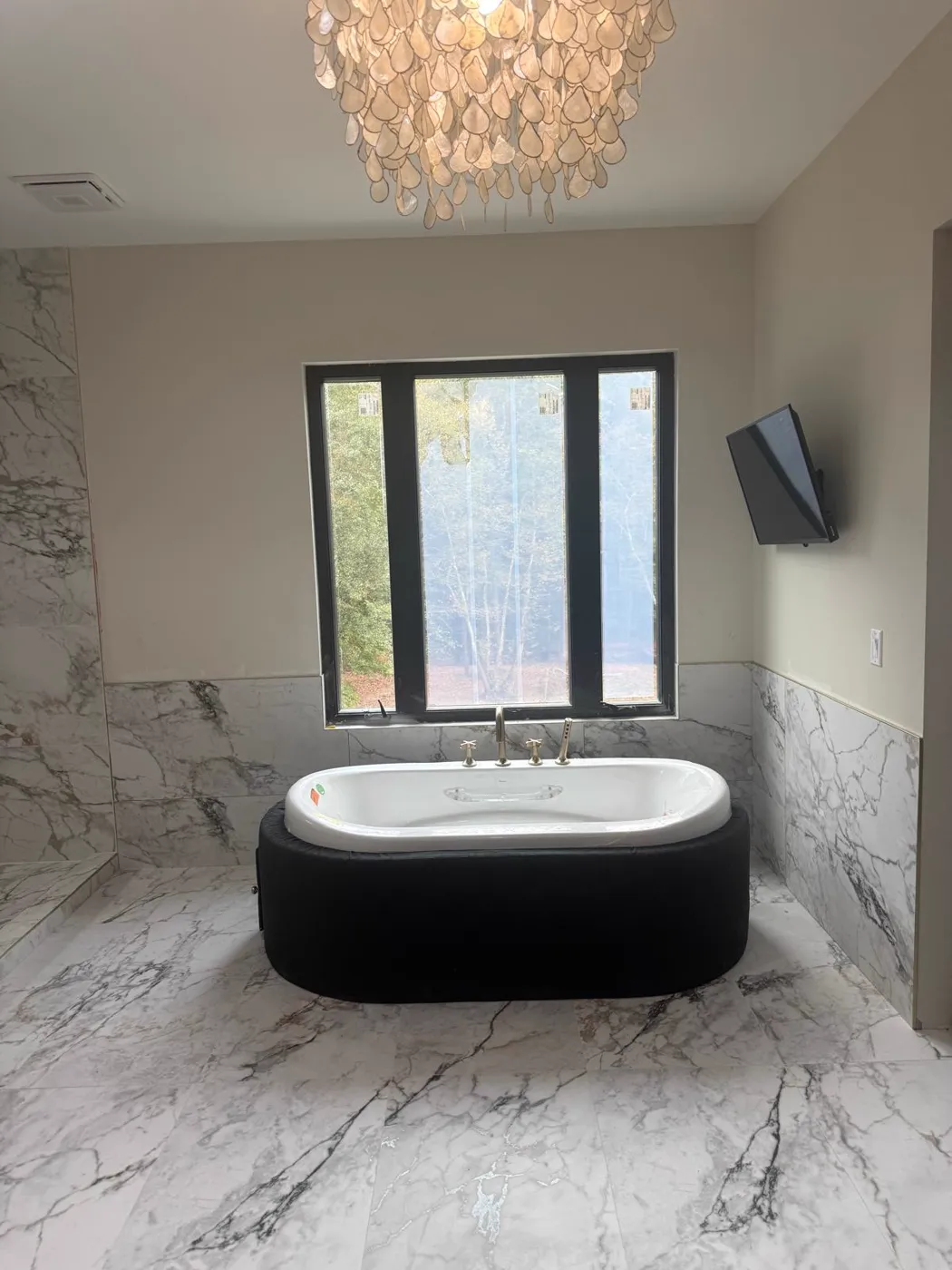 Finished master bathroom with a freestanding tub, full marble-look tile walls and a chandelier, Metro Atlanta