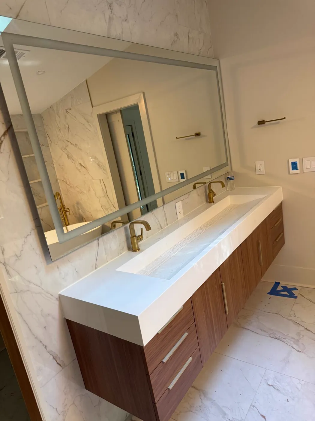 Finished double floating vanity with a trough sink, gold faucets and a framed mirror on marble-look tile, Metro Atlanta